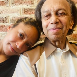 Maria - daughter, brown woman with blonde highlights in hair leaning her head on dad's right shoulder. Dad is a brown man in his 80s with a cream shirt on with brown collars.